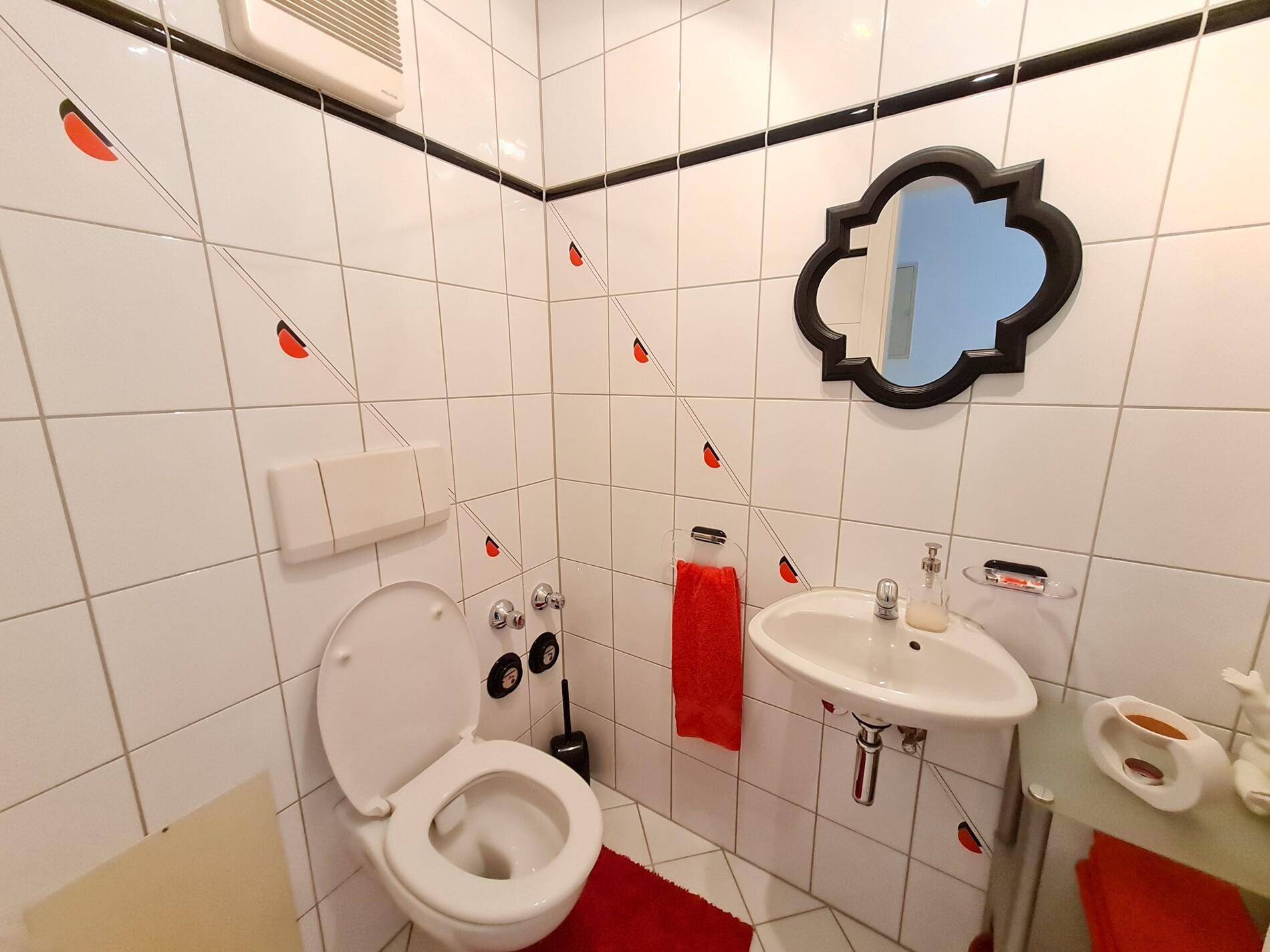 Kleines Gäste-WC mit weißen Fliesen, Eckwaschbecken und einem dekorativen Spiegel.