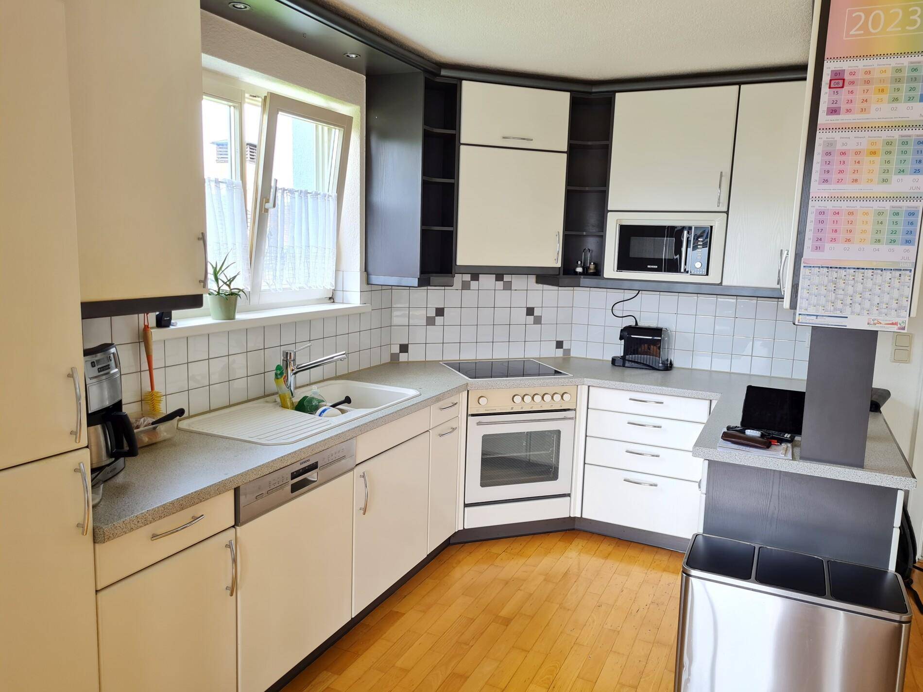 Funktionale Küche mit weißen Schränken, integrierten Geräten und einem Fenster für Tageslicht.