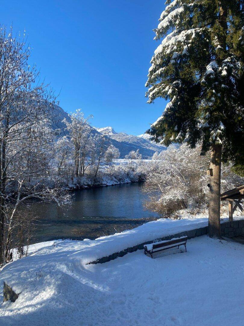 Atemberaubende Winterlandschaft mit klarem blauen Himmel, schneebedeckten Bergen und einem ruhigen Fluss.