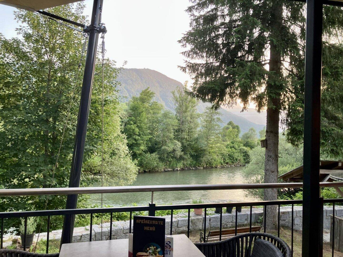Blick von der Terrasse auf den Fluss und die umliegenden Berge in einer grünen Landschaft.