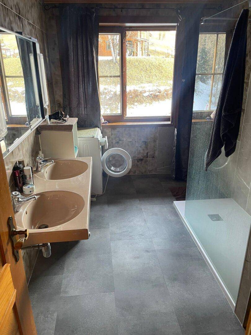 Badezimmer mit Doppelwaschbecken, Duschbereich und Waschmaschine, hell durch ein Fenster.