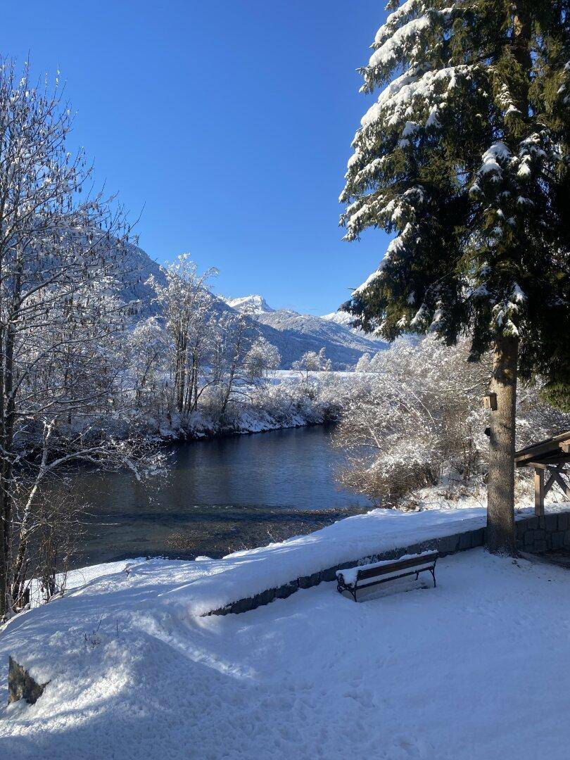 Atemberaubende Winterlandschaft mit klarem blauen Himmel, schneebedeckten Bergen und einem ruhigen Fluss.