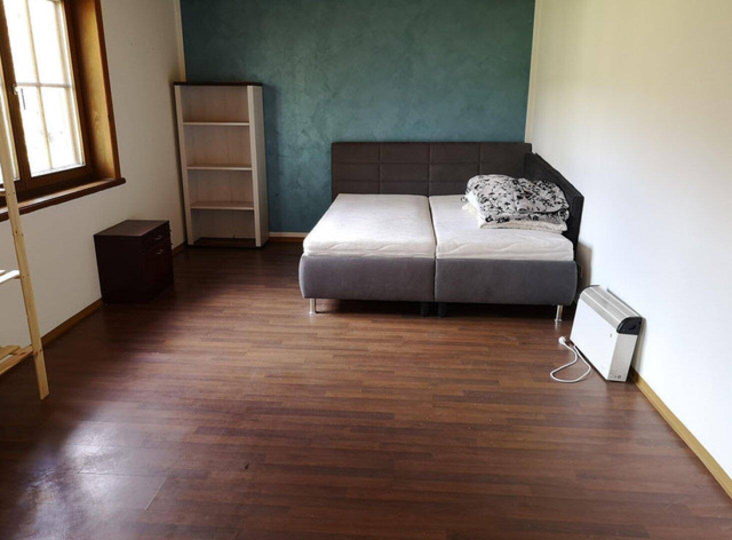 Geräumiges Schlafzimmer mit Holzboden, Doppelbett und einer farbigen Akzentwand.
