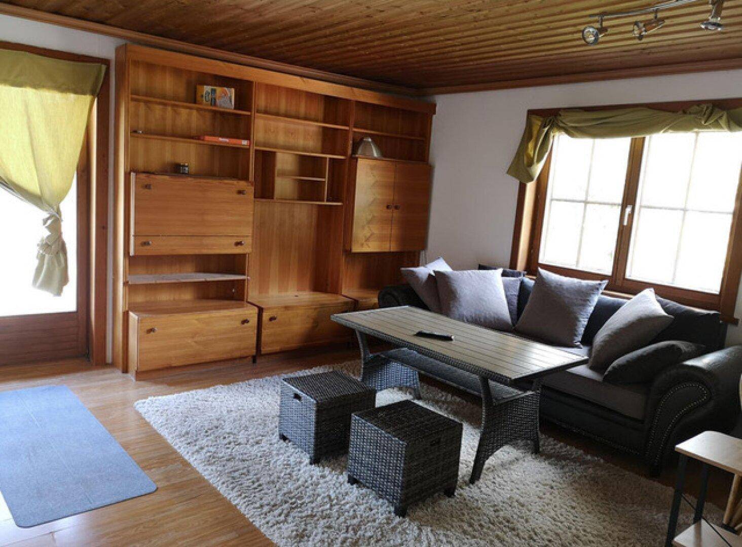 Gemütliches Wohnzimmer mit großer Holzschrankwand, Sofa und Teppichboden.