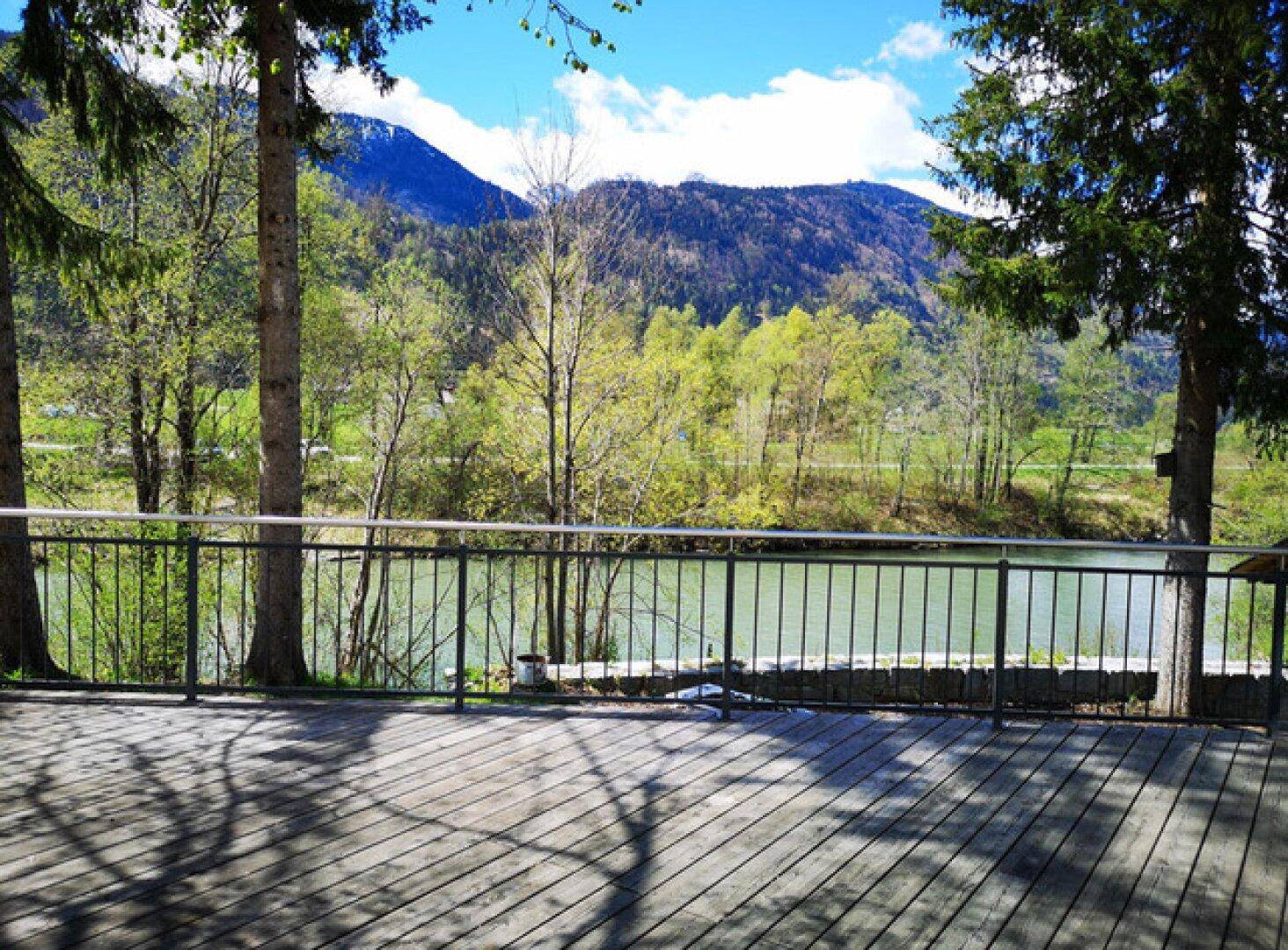 Große Holzterrasse mit Blick auf den Fluss und die grünen Berge an einem sonnigen Tag.