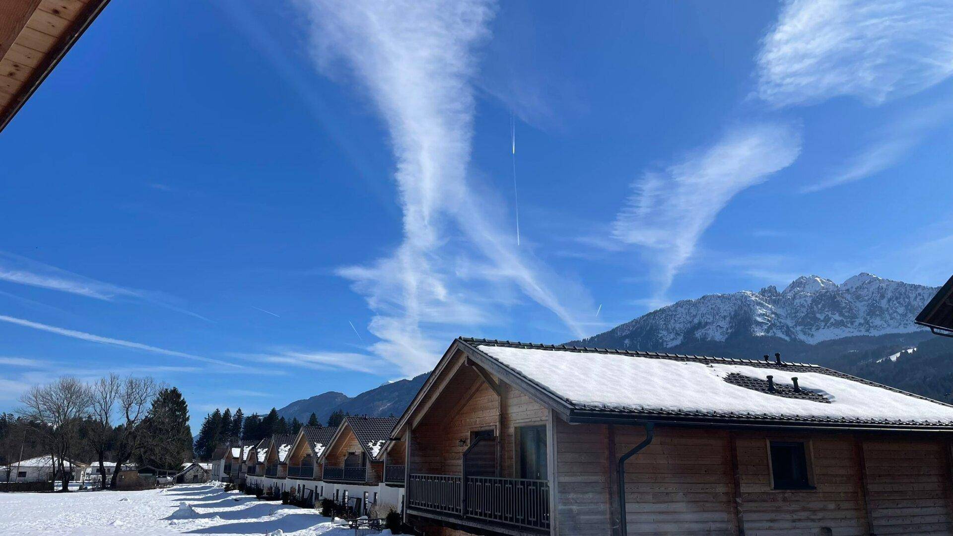 Reihe von charmanten, schneebedeckten Chalets mit Bergblick unter einem klaren Winterhimmel.