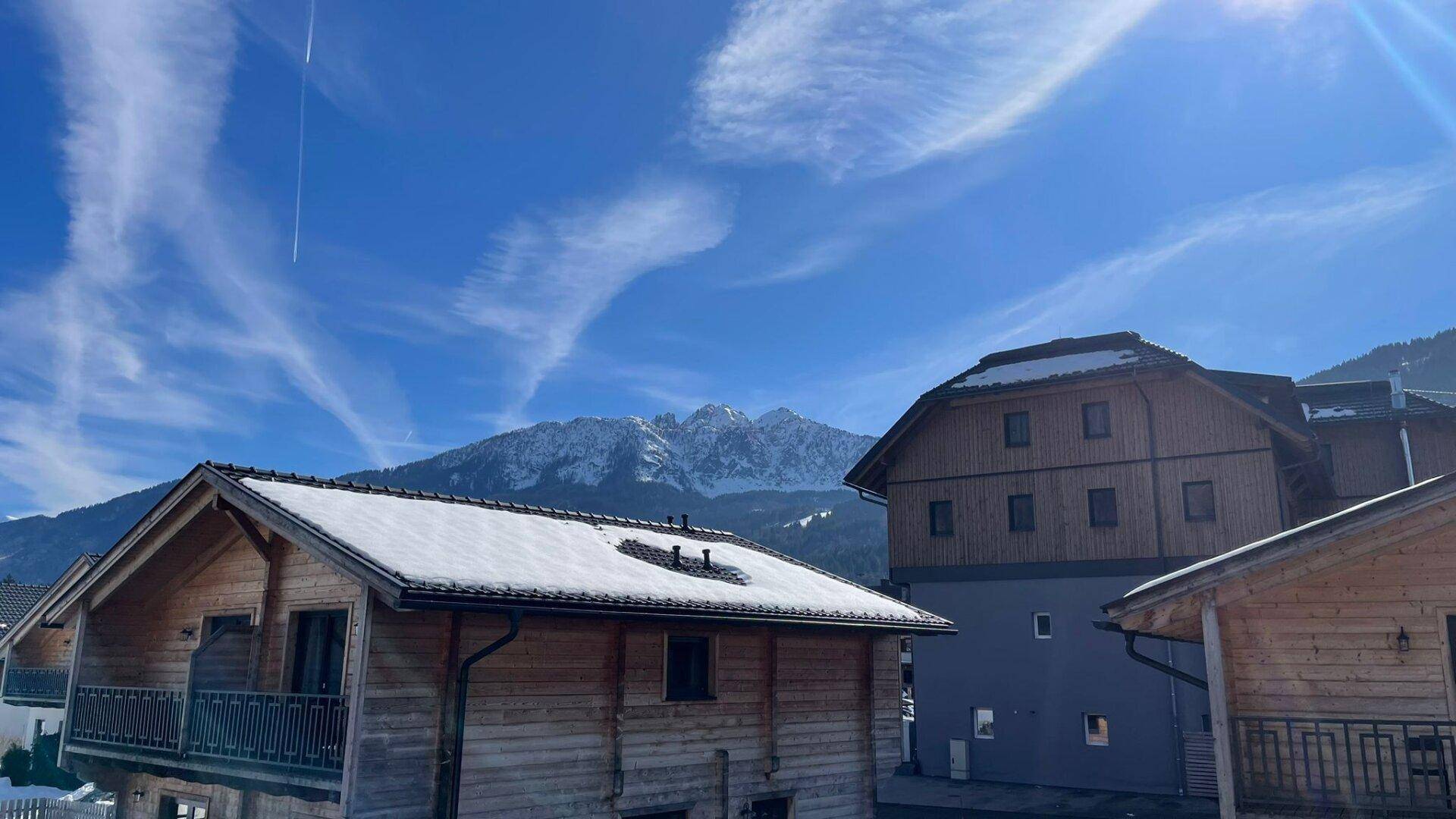 Panoramablick auf schneebedeckte Chalets und majestätische Berge unter einem weiten blauen Himmel.