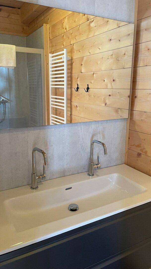 Modernes Badezimmer mit Doppelwaschbecken, großem Spiegel und Holzwänden, inklusive Handtuchheizkörper.