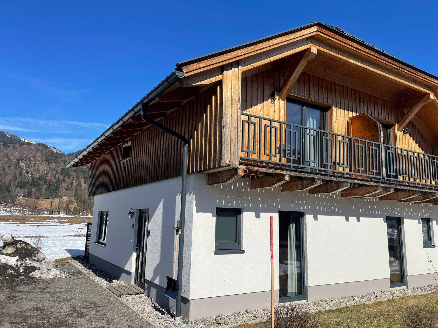 Modernes Chalet-Gebäude mit weißer Fassade, Holzelementen und einem Balkon, umgeben von winterlicher Landschaft.