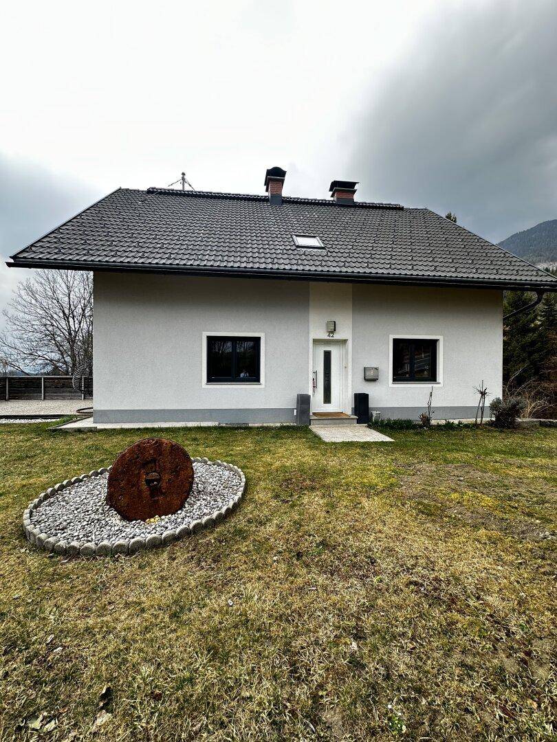 Vorderansicht des Einfamilienhauses mit gepflegtem Vorgarten und Bergblick im Hintergrund.