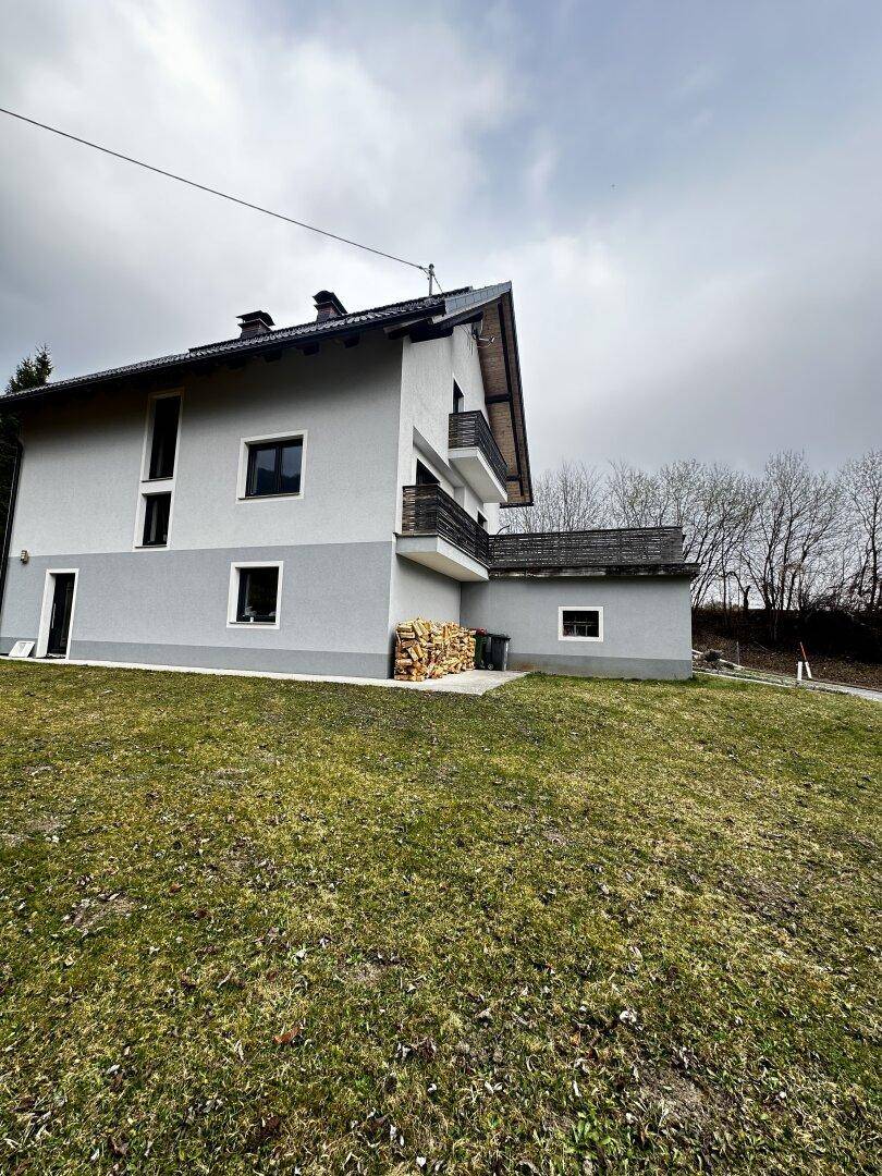 Seitenansicht des Hauses mit gestapeltem Brennholz und Balkon im Obergeschoss.