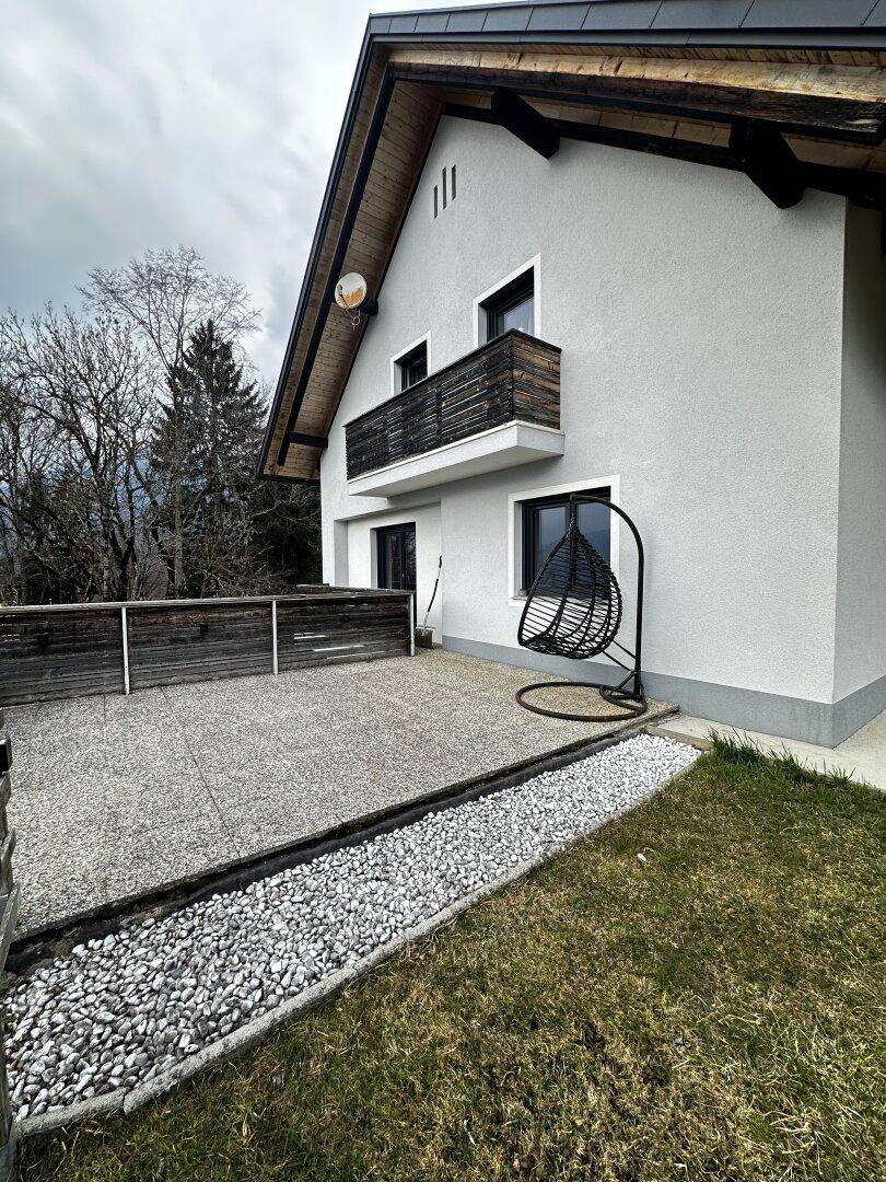 Gepflasterter Terrassenbereich an der Hausseite mit Hängesessel und Holzbalkon.
