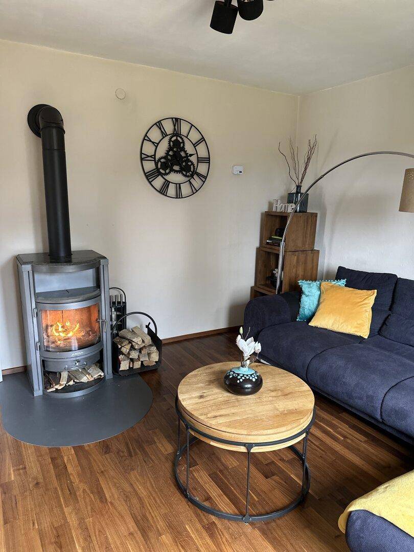 Gemütliches Wohnzimmer mit Holzboden, modernem Kaminofen und bequemer Couch.