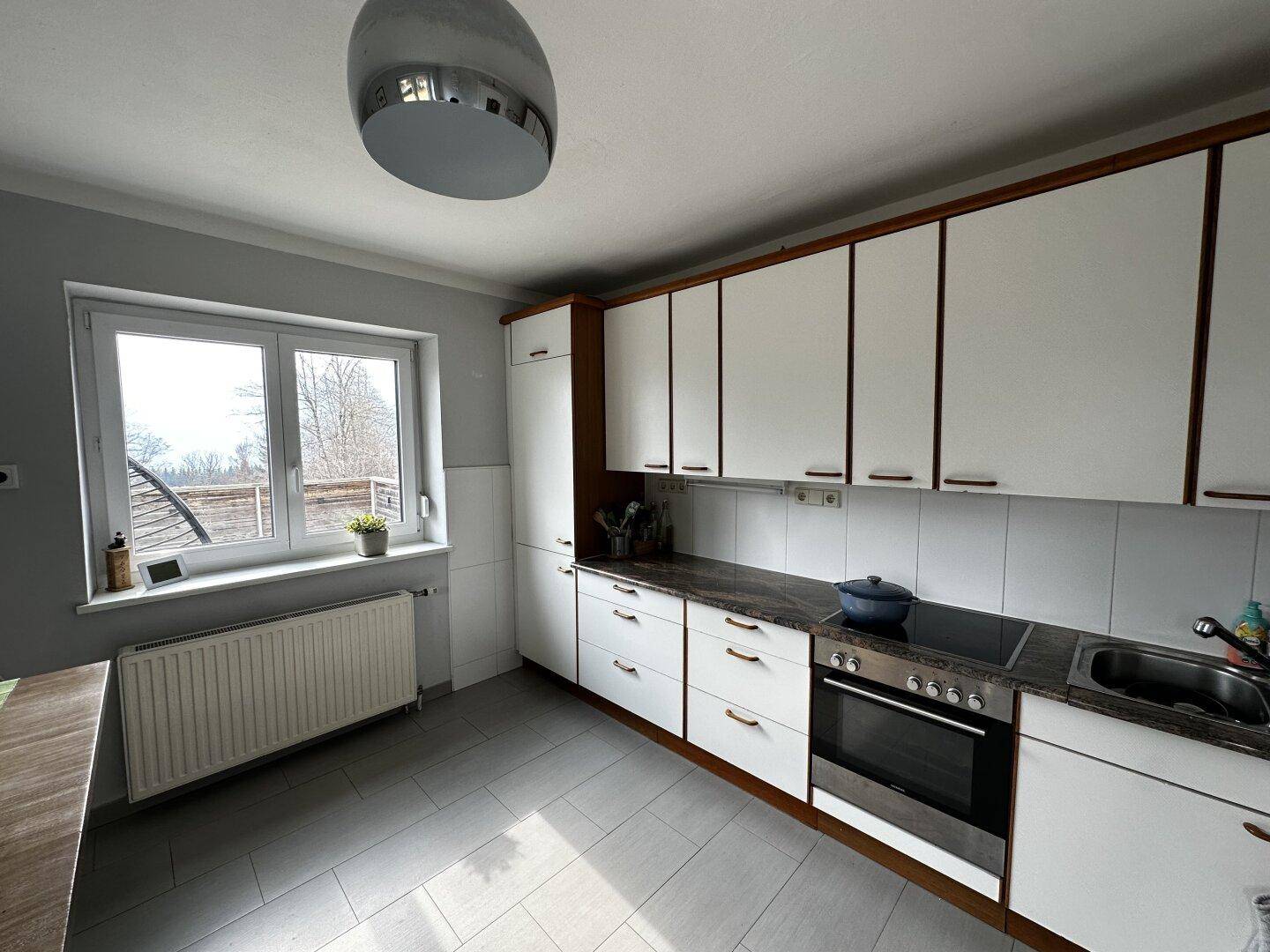 Funktionale Küche mit weißen Schränken, Fliesenboden und Fenster.