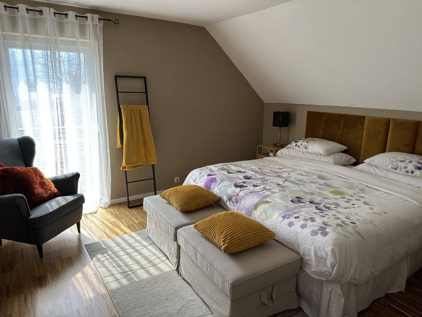 Helles Schlafzimmer mit Doppelbett, Holzboden und Zugang zum Balkon.