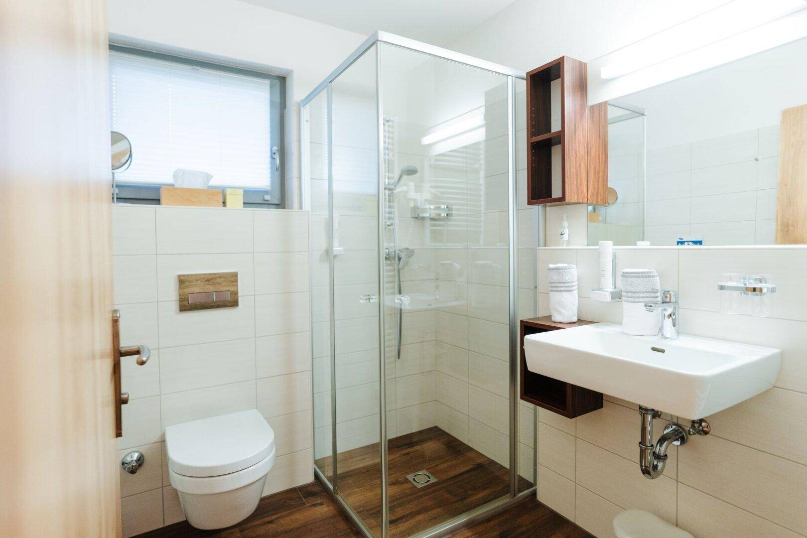 Helles Badezimmer mit Dusche, wandhängendem WC, Waschbecken und Fenster für Tageslicht.