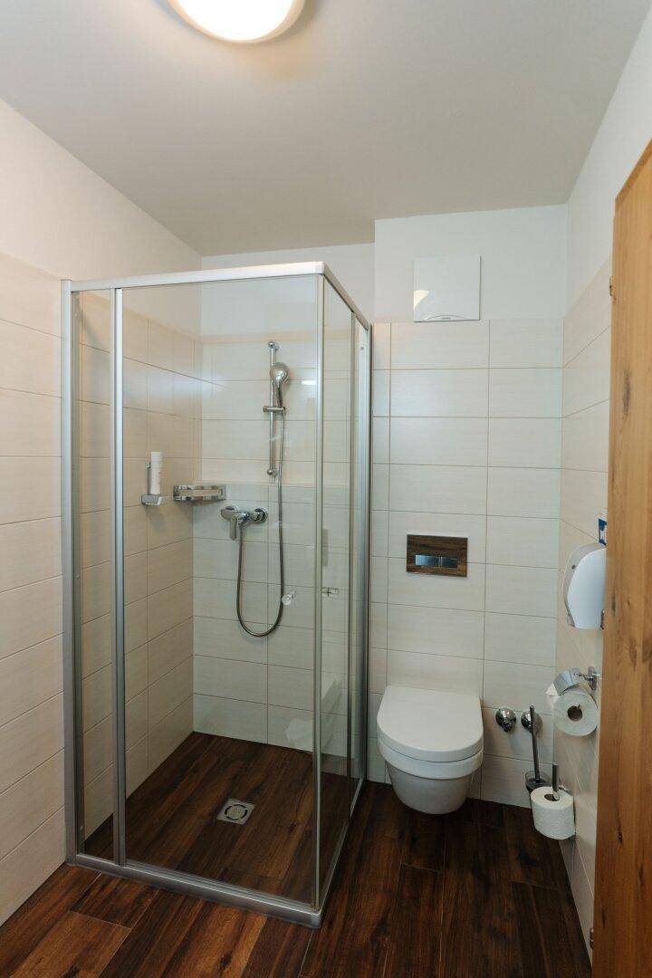 Modernes Badezimmer mit Duschkabine und wandhängendem WC auf dunklem Holzimitatboden.