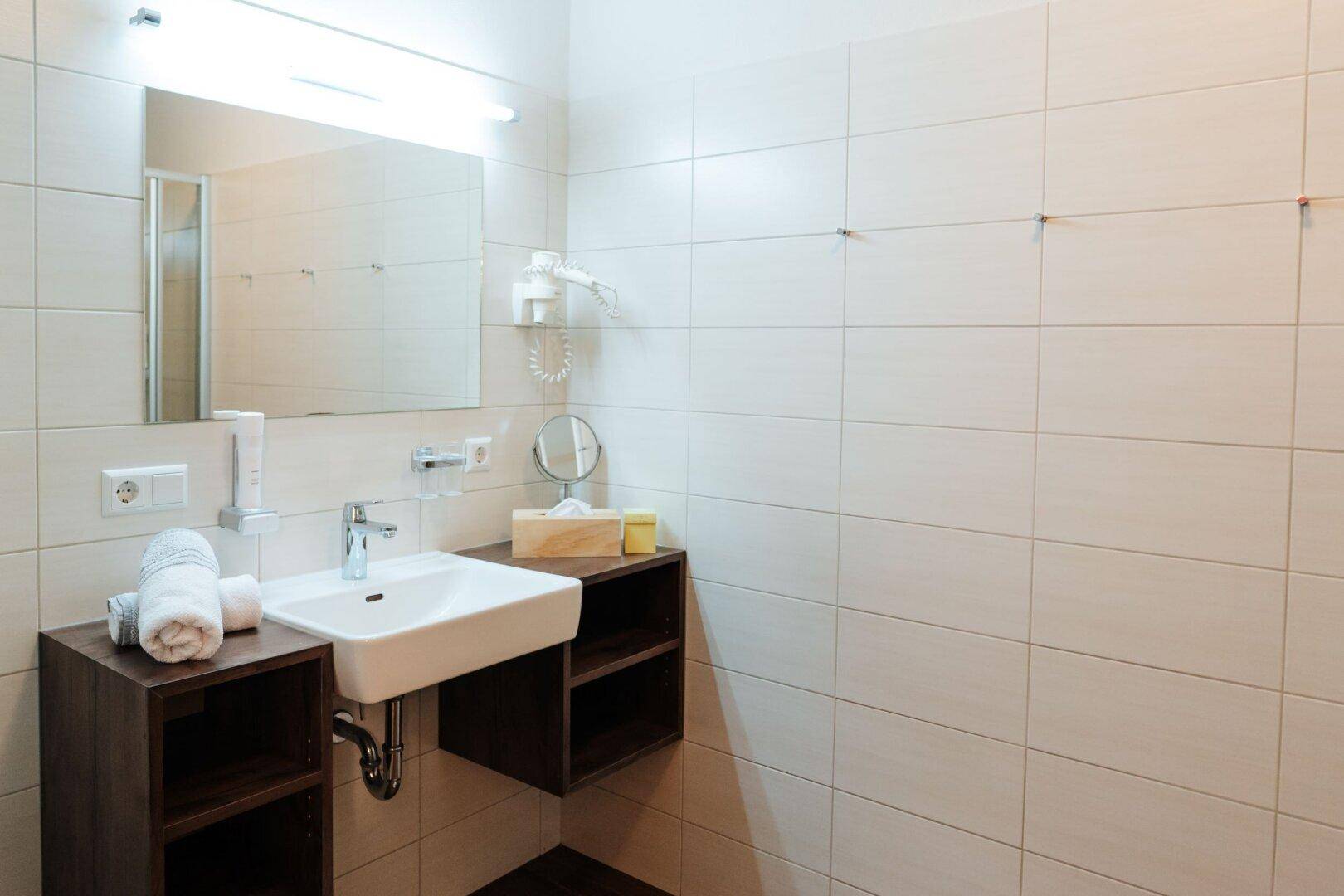 Badezimmer mit Waschbecken, großem Spiegel und hellen Fliesen an den Wänden.