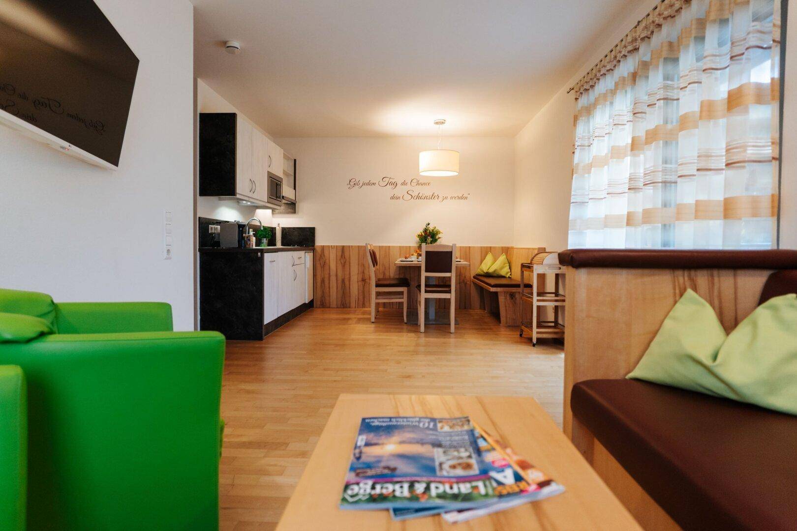Geräumiger Wohn- und Essbereich mit Küchenzeile, Holzboden und grünen Akzenten im Sofa.