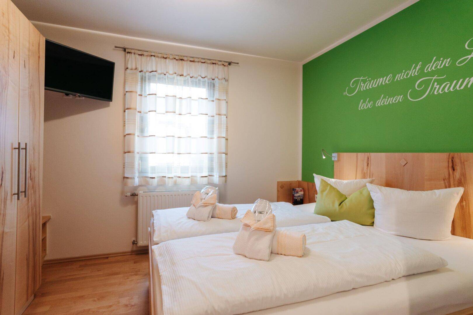 Schlafzimmer mit Doppelbett, grün gestrichener Akzentwand und Holzkleiderschrank.