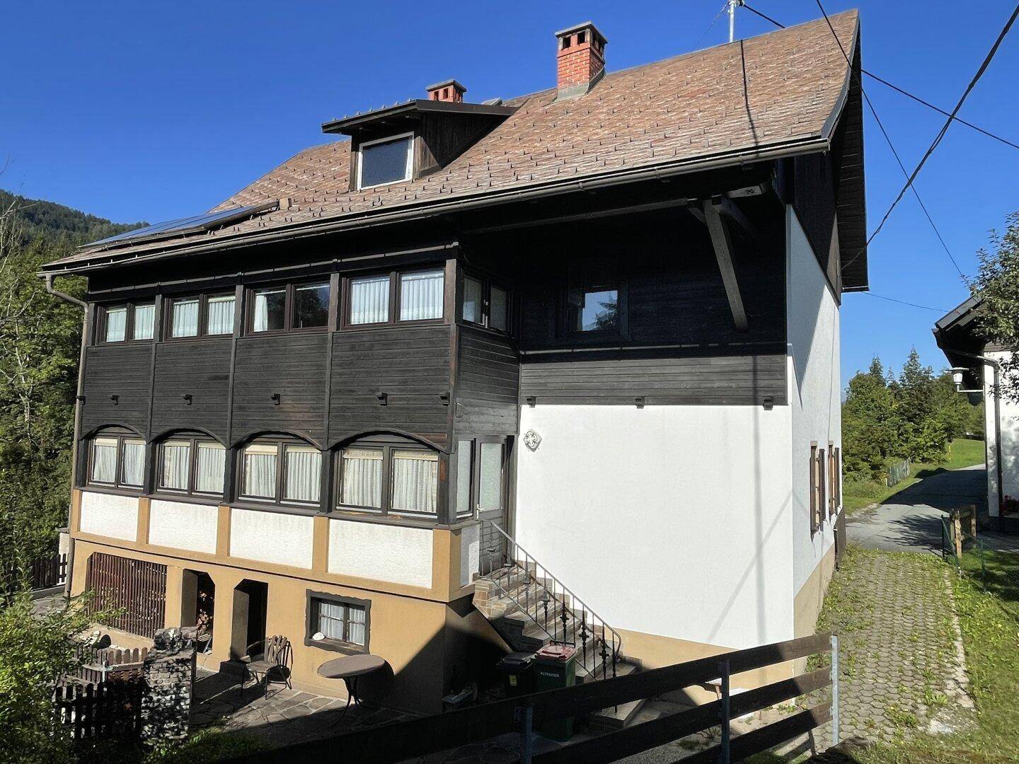 Ansicht eines traditionellen Hauses mit dunkler Holzverkleidung, weißen Wänden und Außentreppe.