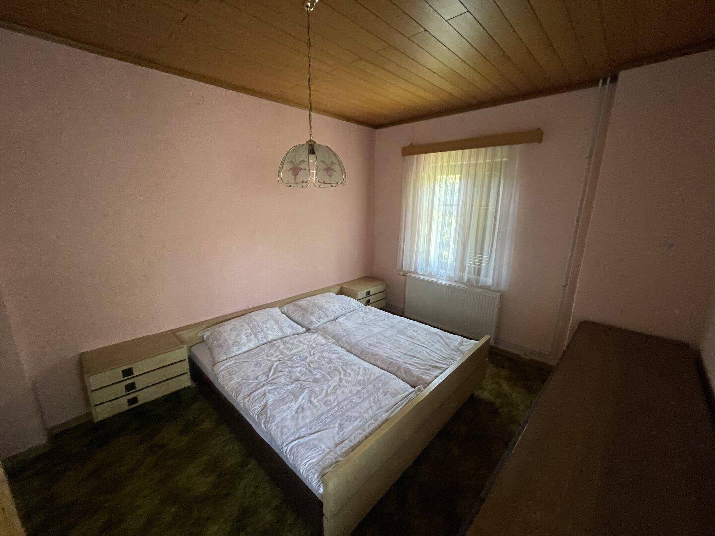 Gemütliches Schlafzimmer mit rosa Wänden, Holzdecke und einem Doppelbett.