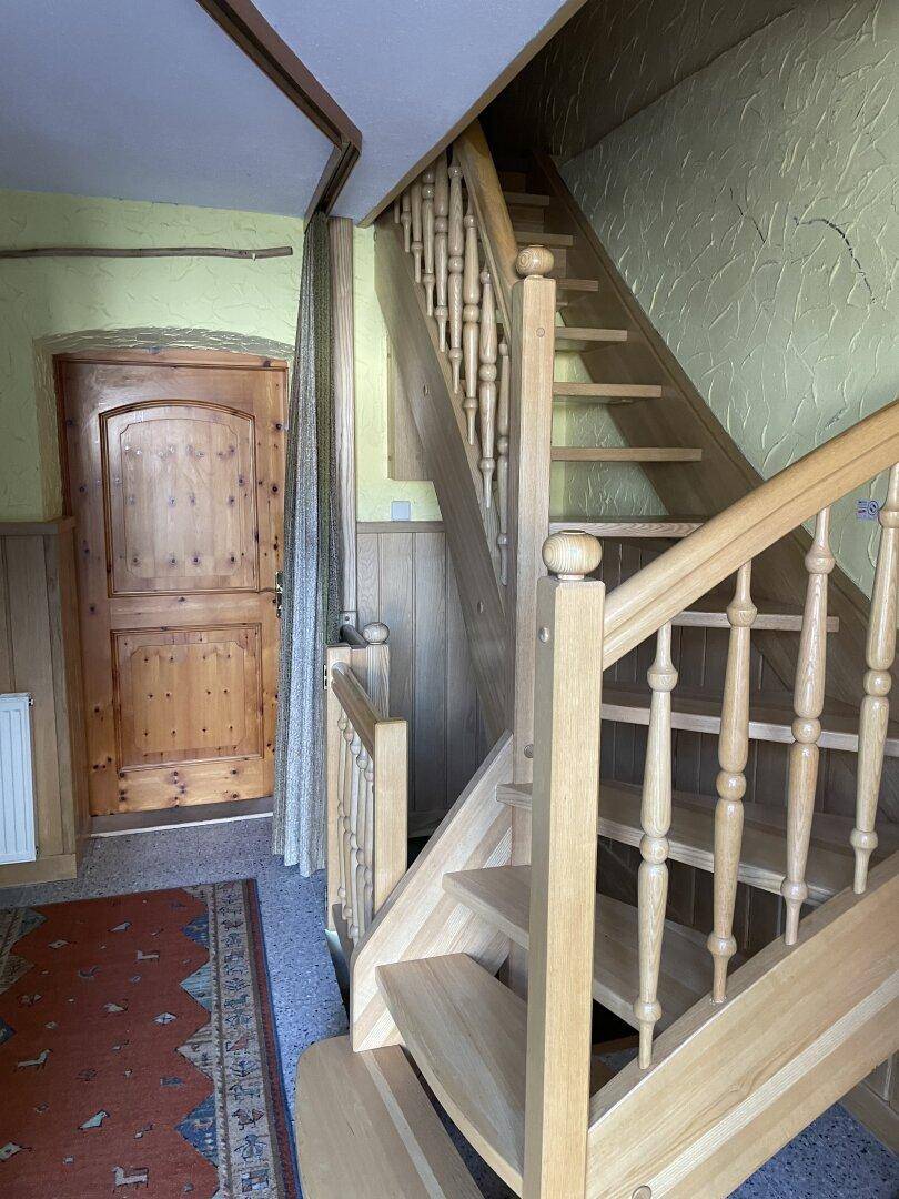 Heller Flur mit Holztreppe, Teppichboden und einer Holztür.