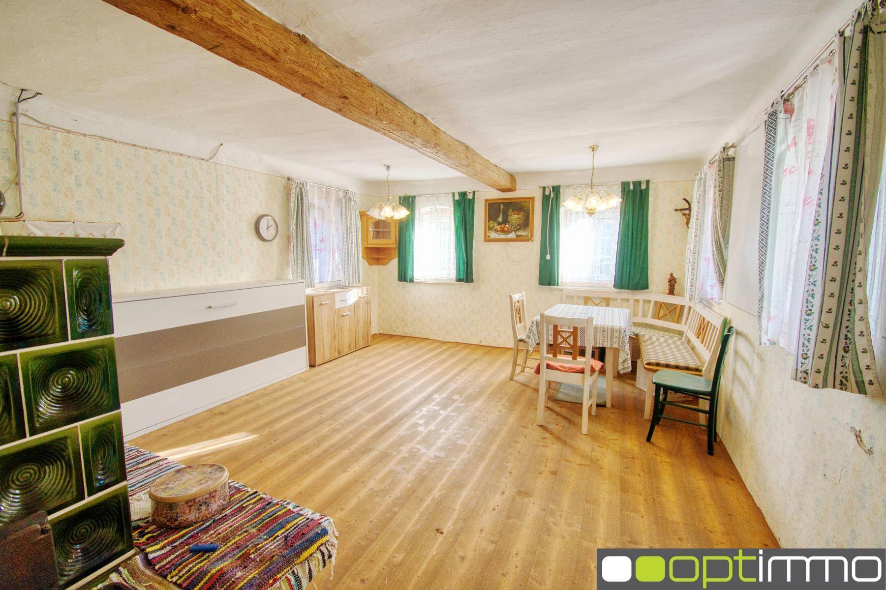 Heller Wohn-Essbereich mit Holzboden, sichtbaren Deckenbalken und traditionellem Kachelofen.