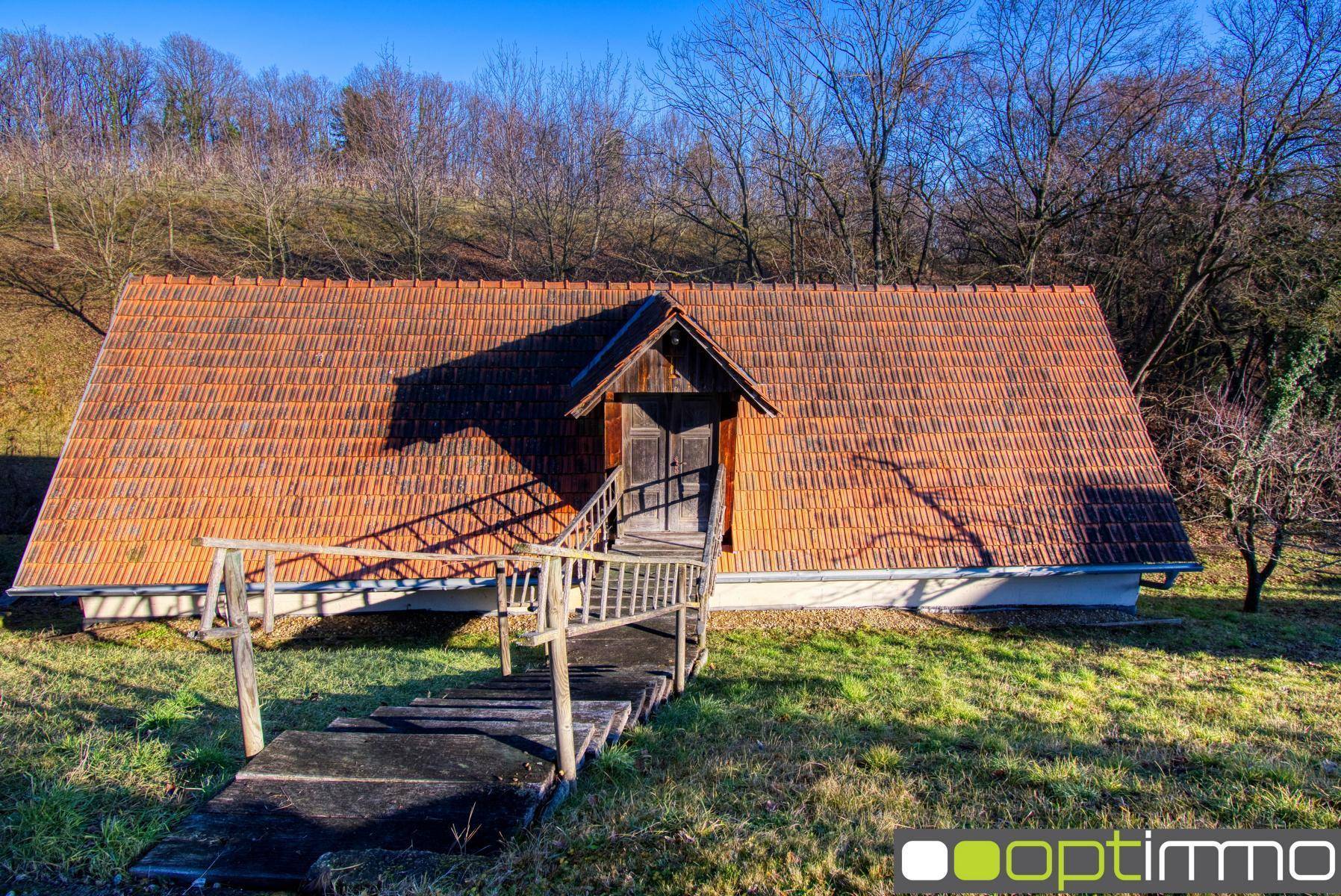 Ländliches Nebengebäude mit rotem Ziegeldach und rustikalem Holzsteg in grüner Umgebung.