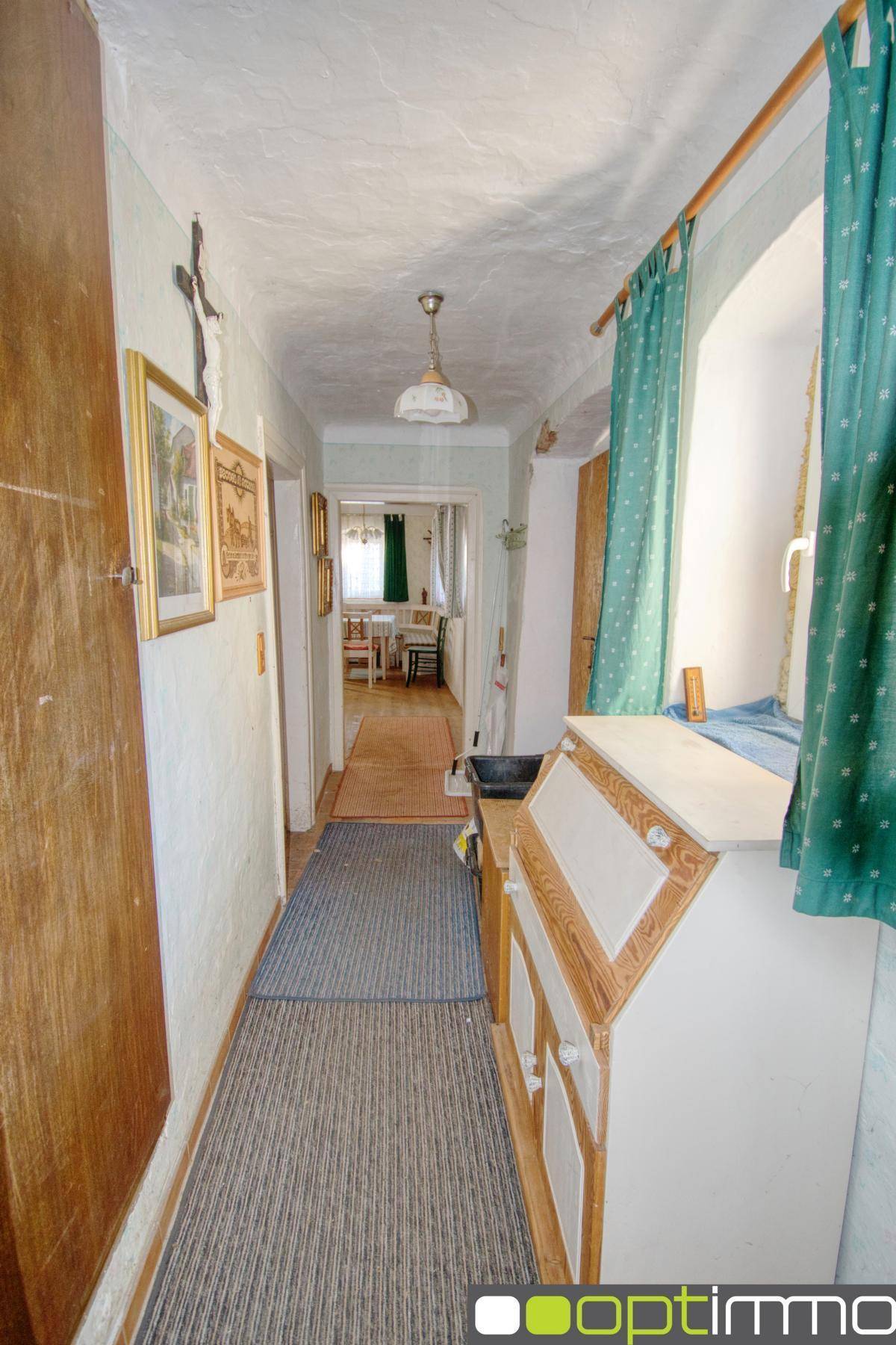 Schmaler Flur mit Teppichboden, Holzmöbeln und natürlichem Lichteinfall durch Fenster.