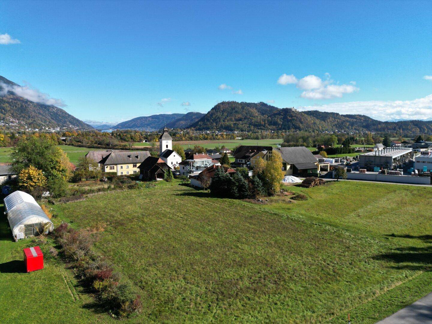 Weitläufige Luftaufnahme einer ländlichen Gegend mit grünen Feldern, Häusern und Bergen am Horizont.