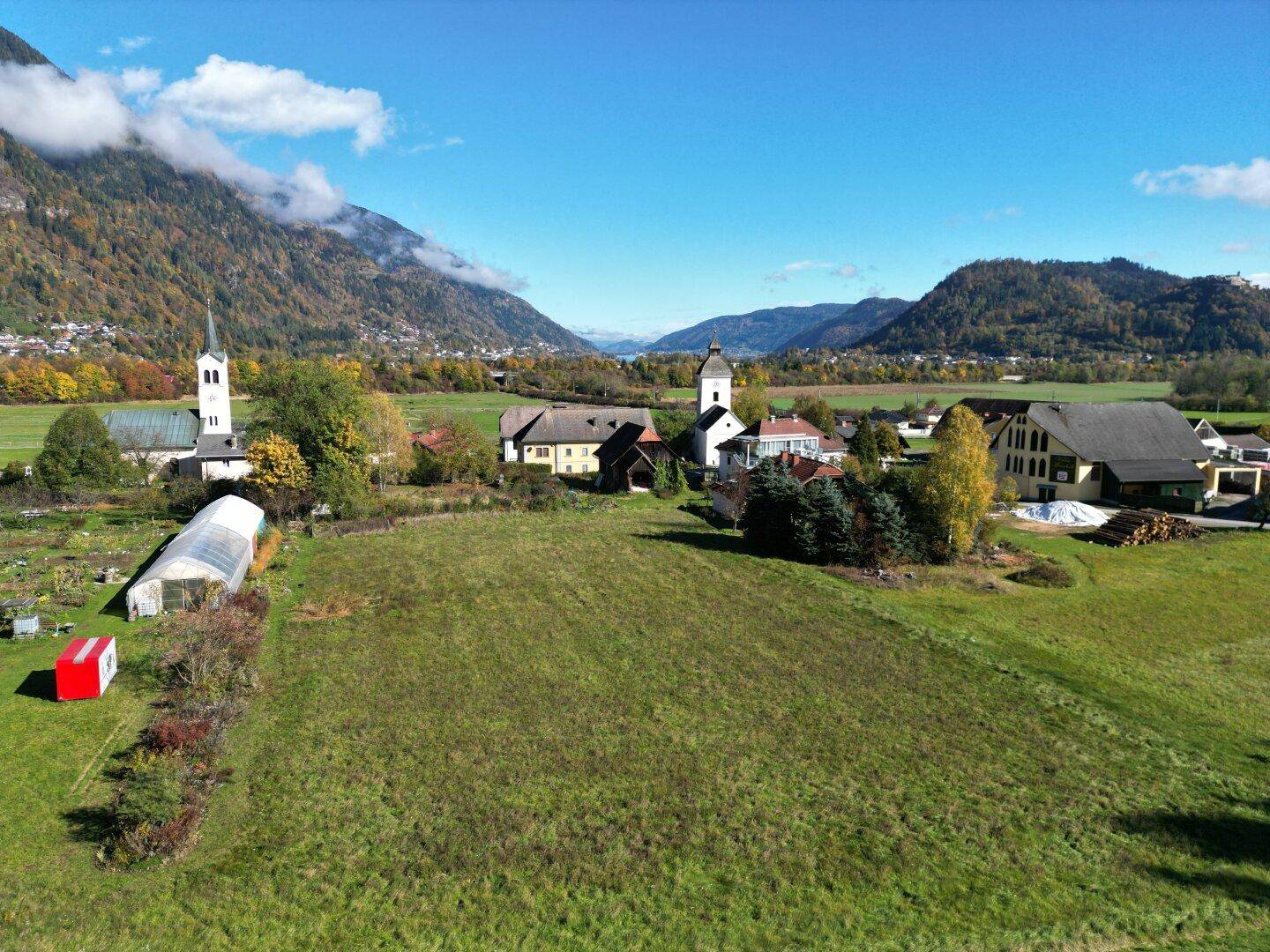 Panoramablick auf ein großes grünes Grundstück, umgeben von ländlicher Bebauung und einer beeindruckenden Bergkulisse.
