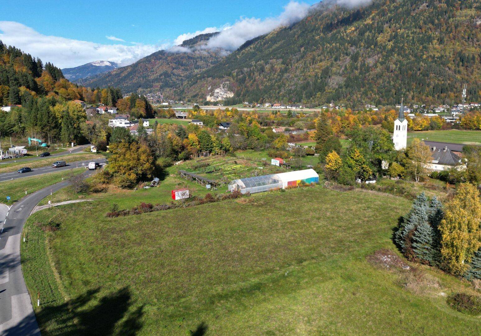 Luftaufnahme eines Grundstücks mit angrenzender Straße, umgeben von herbstlicher Natur und Berglandschaft.
