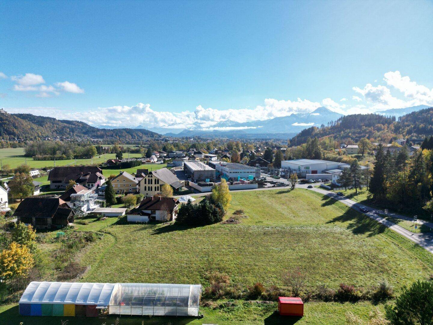 Luftaufnahme eines großen Grundstücks mit Blick auf ein Dorf und schneebedeckte Berge in der Ferne.