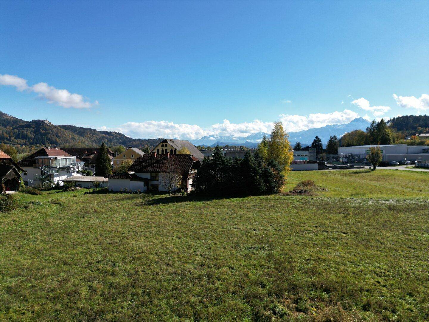 Luftaufnahme eines großen Grundstücks mit Blick auf ein Dorf und schneebedeckte Berge in der Ferne.