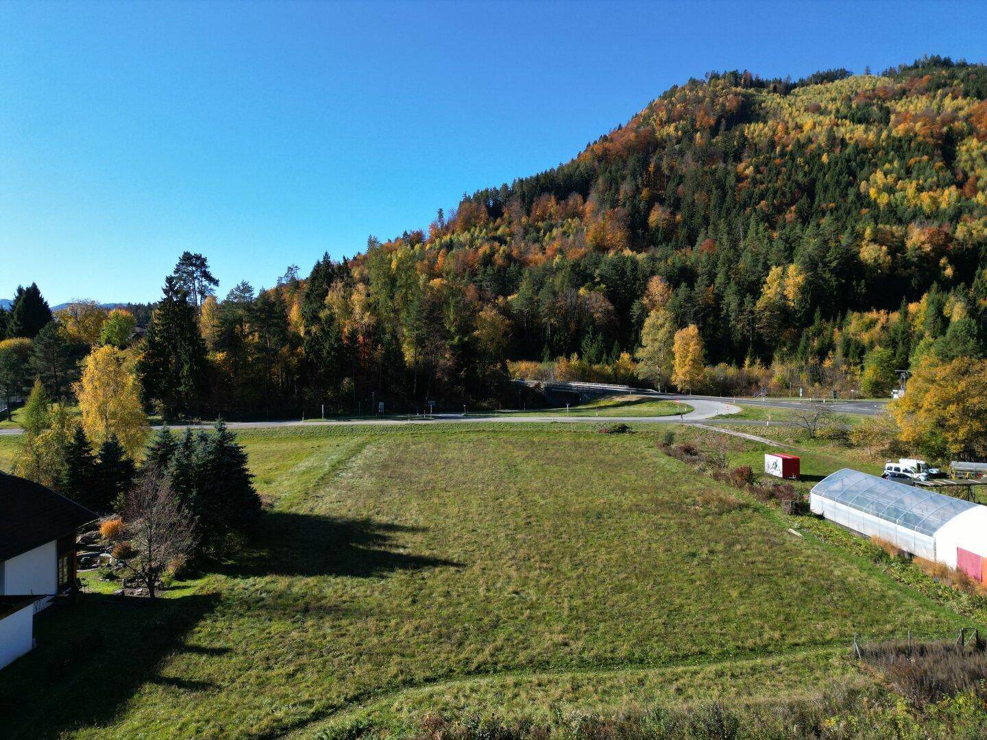 Luftaufnahme eines weitläufigen Feldes mit einer kurvigen Straße und einem bewaldeten Berg in Herbstfarben.