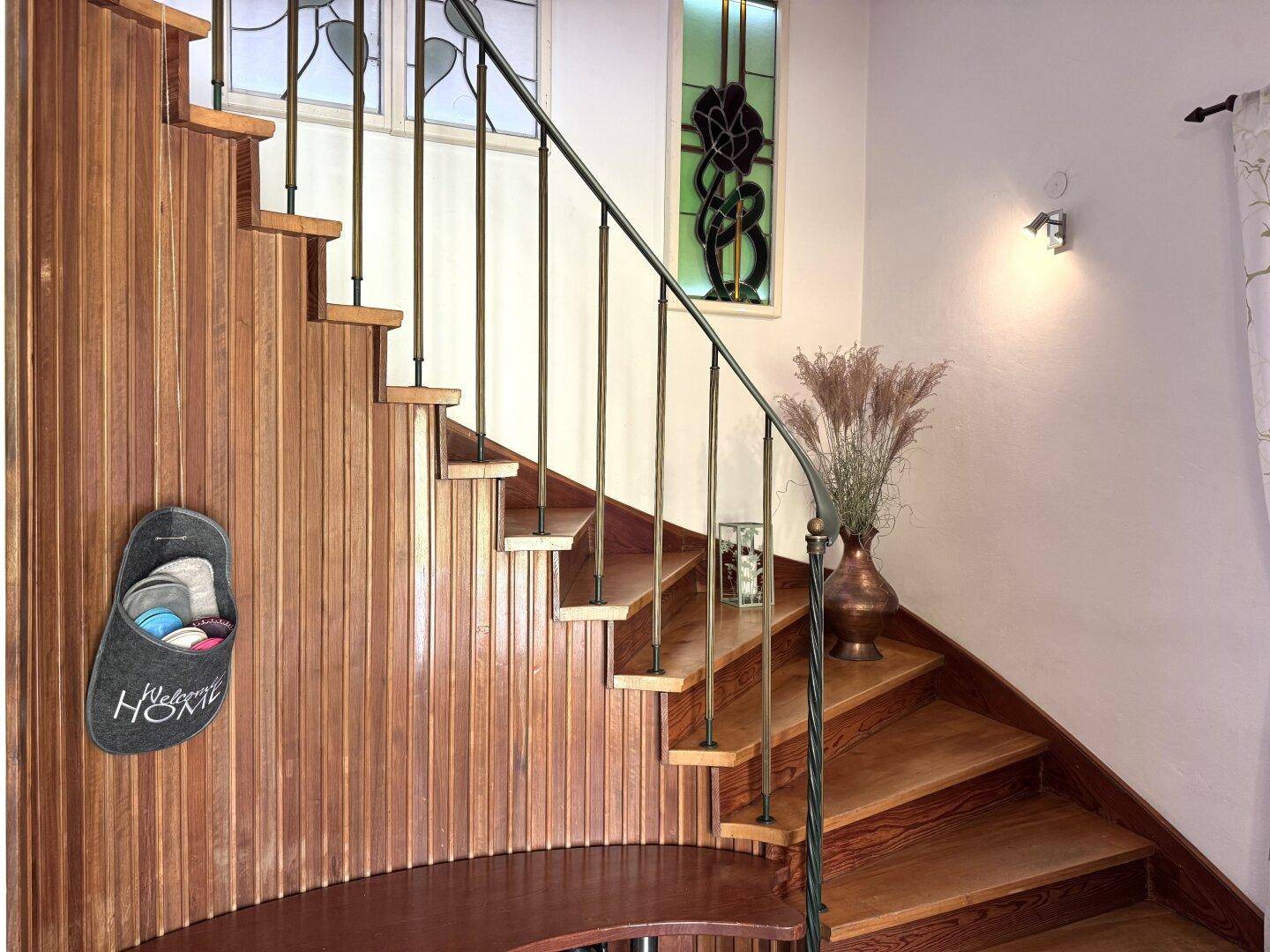 Elegante Holztreppe mit schmiedeeisernem Geländer und dekorativen Buntglasfenstern.