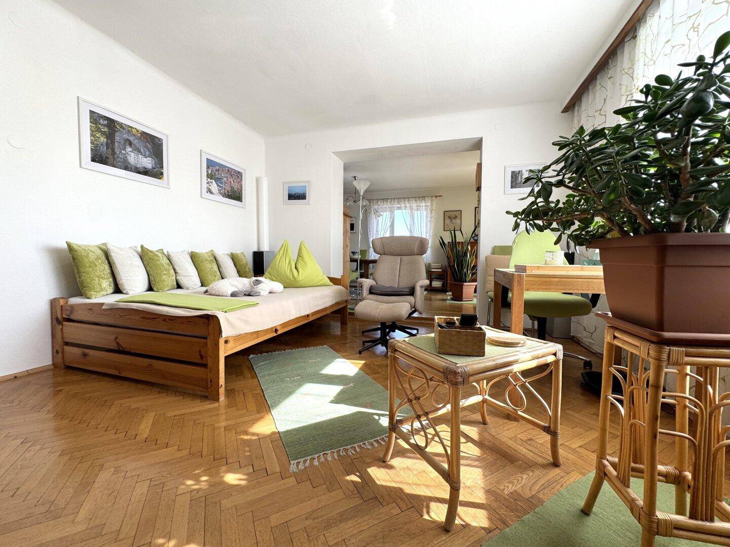 Geräumiges Wohnzimmer mit Tagesbett, Rattanmöbeln und hellem Parkettboden.