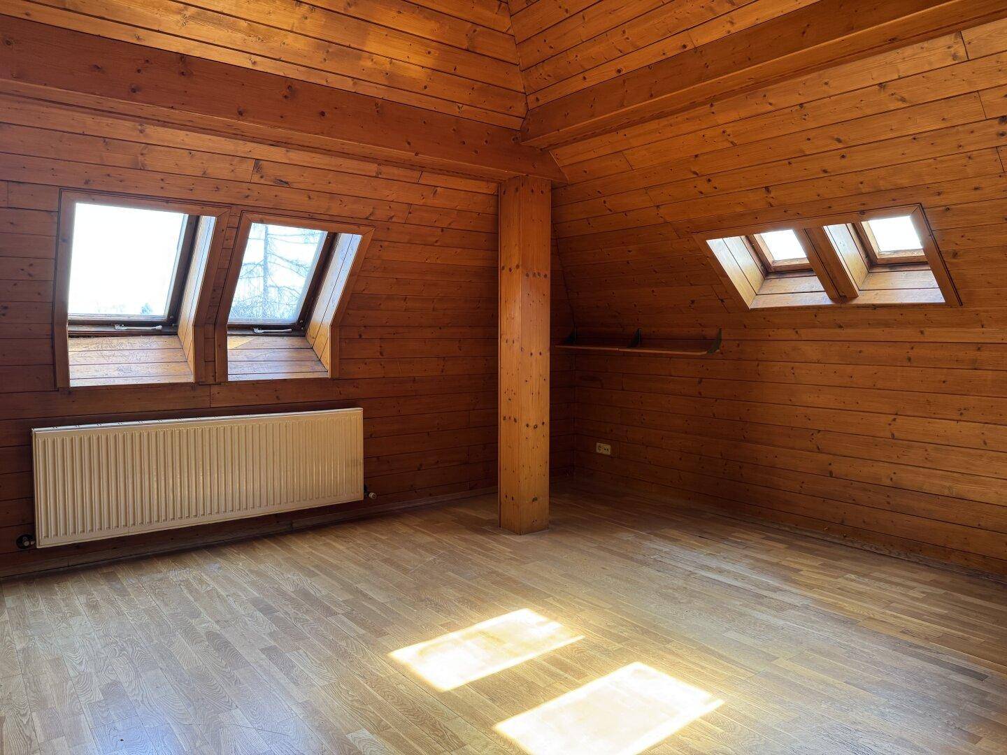 Gemütlicher Dachbodenraum mit Holzverkleidung, Dachfenstern und Heizkörper.