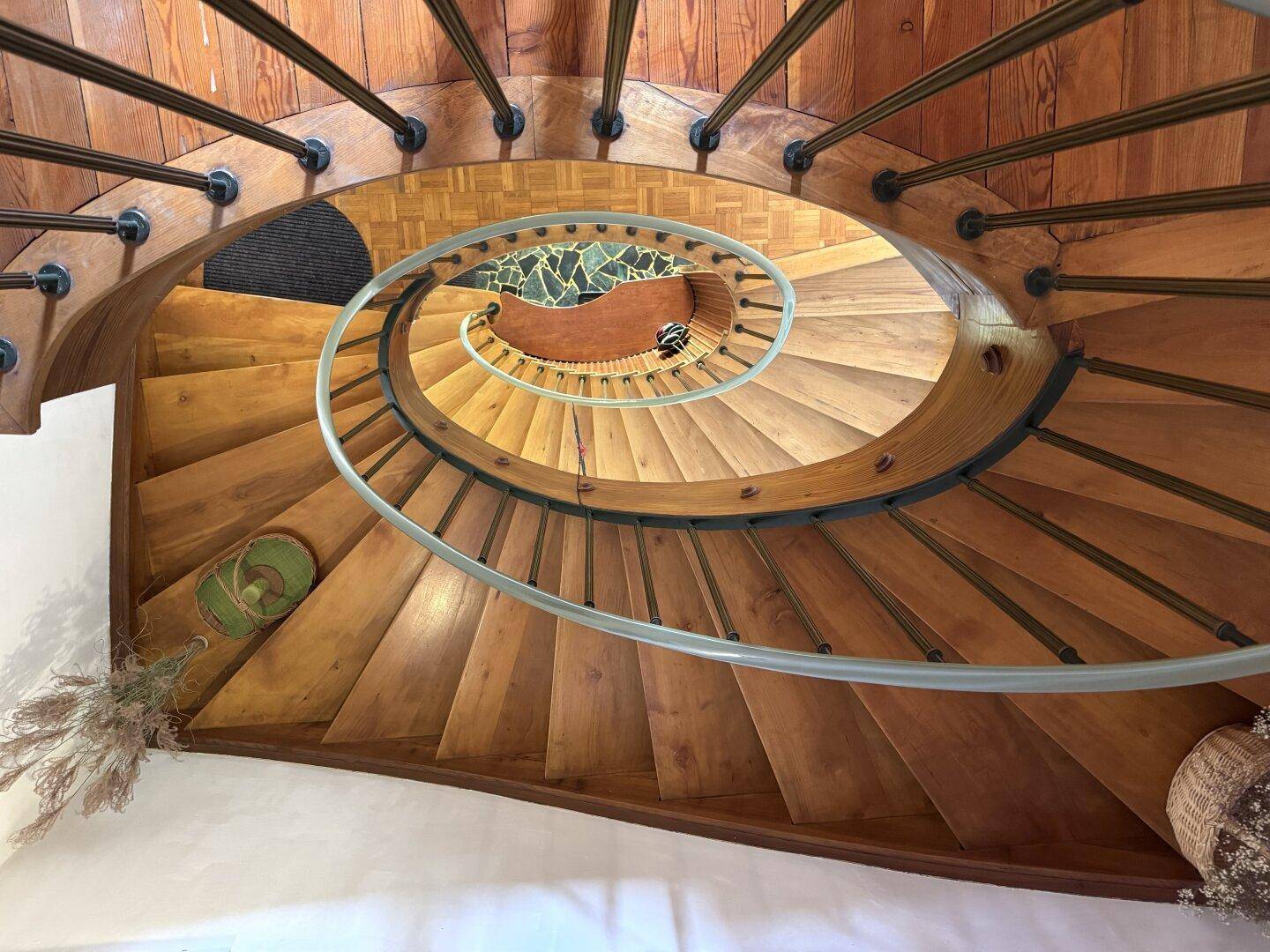 Elegante Wendeltreppe aus Holz mit schmiedeeisernem Geländer und dekorativem Boden.