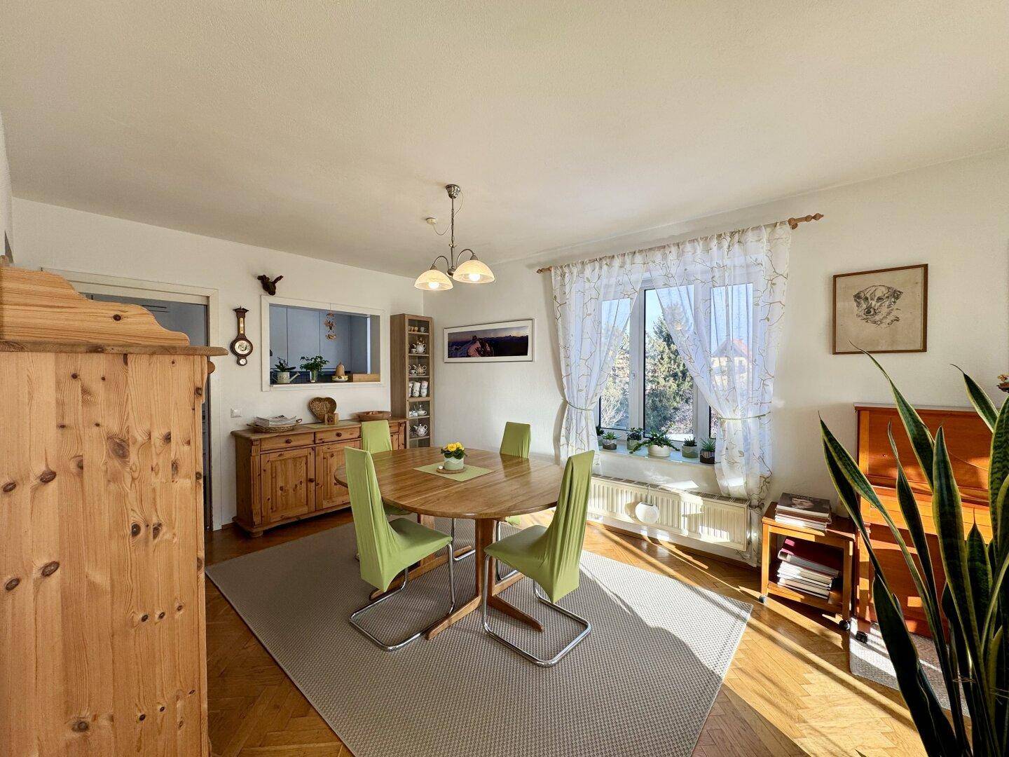 Sonniger Essbereich mit Holztisch, traditionellem Sideboard und Blick ins Grüne.