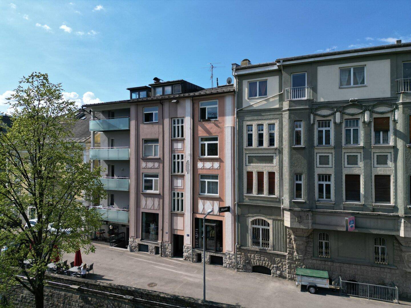 Nahaufnahme der Fassaden von Mehrfamilienhäusern mit Balkonen und Geschäften im Erdgeschoss.