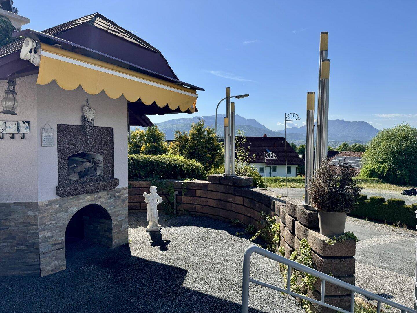Außenbereich mit Steinstruktur, Markise und Skulptur, bietet einen weiten Blick auf die umliegende Berglandschaft.