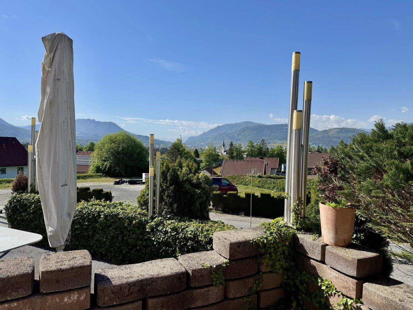 Panoramablick auf die Berglandschaft und umliegende Häuser von einem erhöhten Außenbereich mit Sonnenschirm.