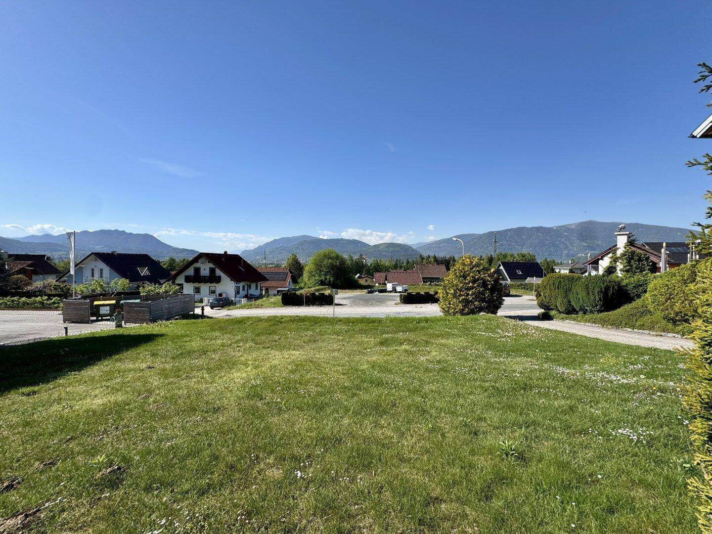 Weitläufige Rasenfläche mit Blick auf die umliegende Wohnbebauung und die dahinterliegenden Berge unter klarem Himmel.