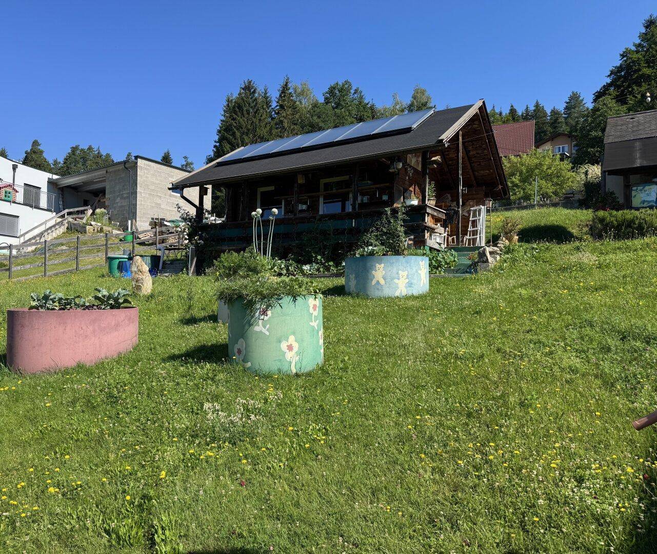Rustikales Gartenhaus mit Photovoltaikanlage auf dem Dach und bunten Pflanzkübeln.