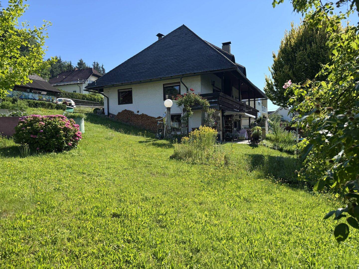 Hausansicht von der Seite mit weitläufiger Rasenfläche und blühenden Hortensien im Vordergrund.