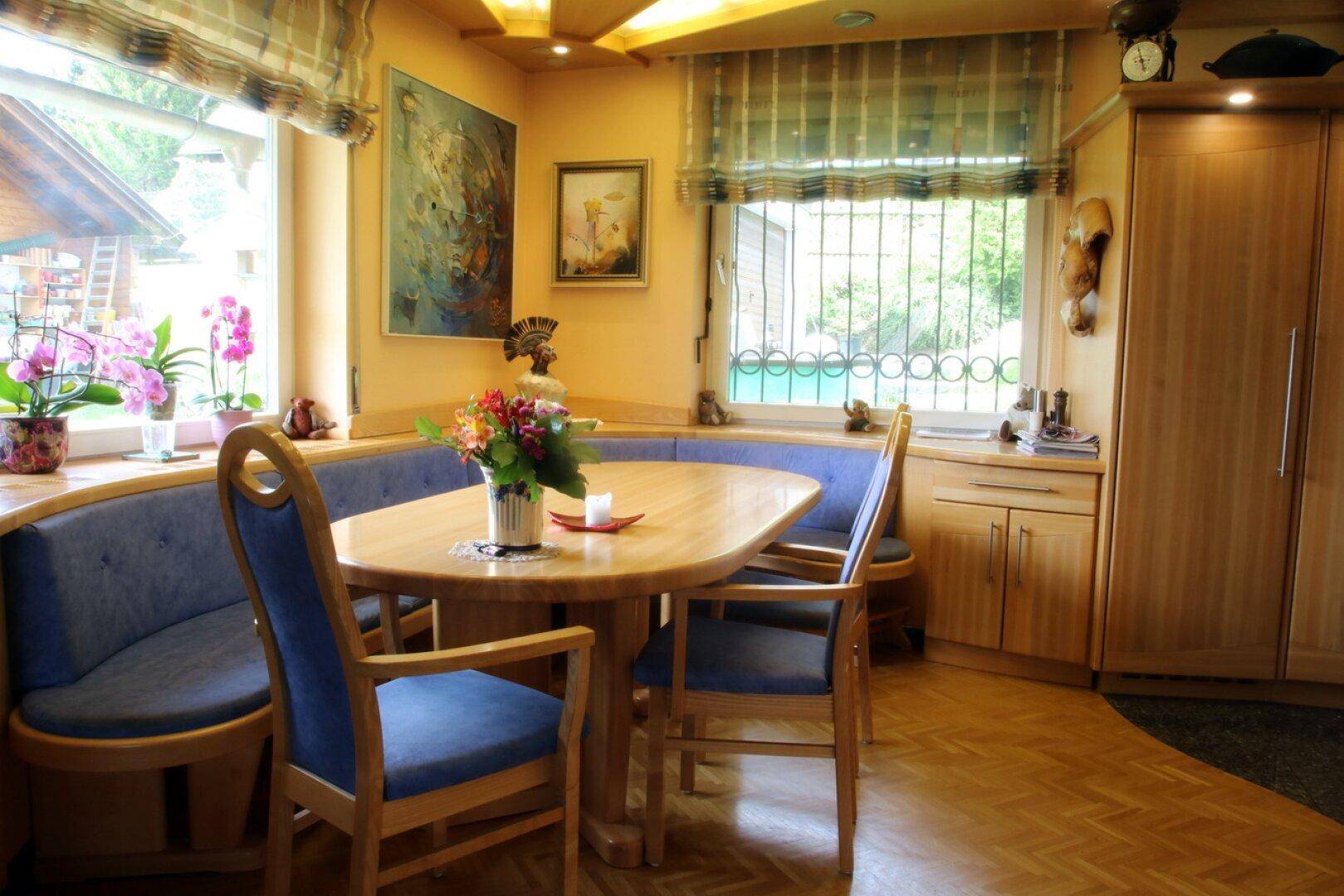 Gemütliche Essecke in der Küche mit Holztisch, blauen Polsterbänken und Fensterblick.
