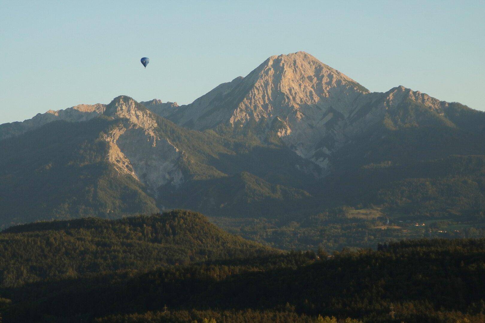 Weitläufige Berglandschaft mit bewaldeten Hügeln unter klarem Himmel und einem Heißluftballon.