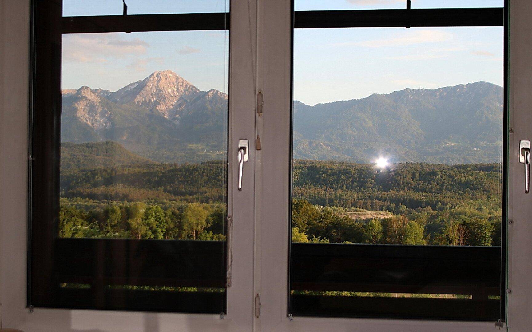 Malerischer Ausblick aus dem Fenster auf eine weite Berglandschaft und grüne Wälder.